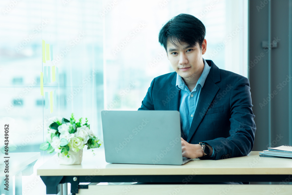 Business portrait - Asian young businessman sitting in an office working with a laptop computer. young age, middle age, a mid adult man in his 20s with a happy confident smile. Copy space. Business portrait - Asian young businessman sitting in an office working with a laptop computer. young age, middle age, a mid adult man in his 20s with a happy confident smile. Copy space.