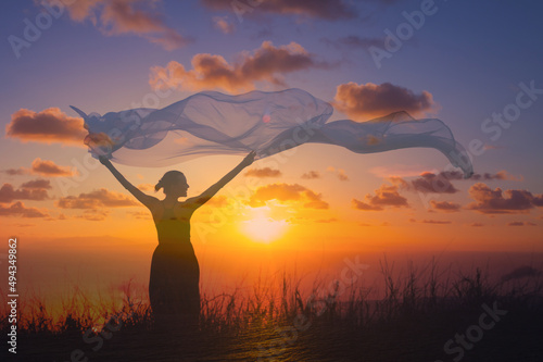 silhouette of a woman in the sunset holding silk cloth blowing in the wind 