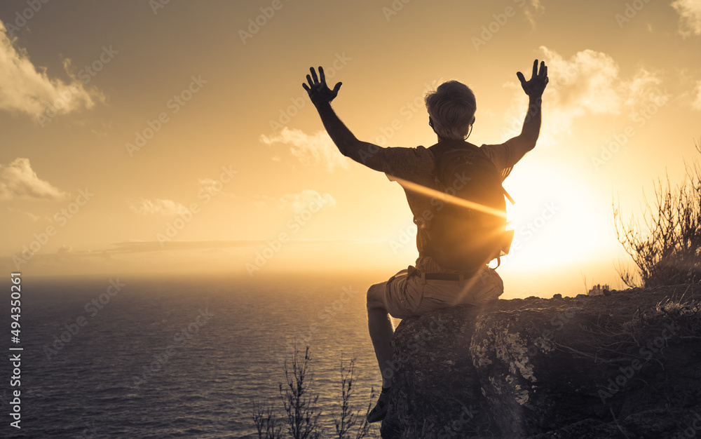 Man sitting on mountain edge with hands up to the light. Feelings of hope and empowerment 