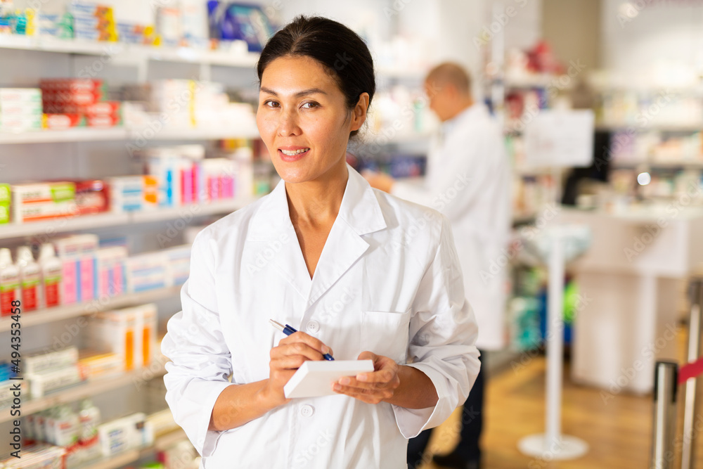 Positive female pharmacist makes notes on a notebook in the sales area of a pharmacy