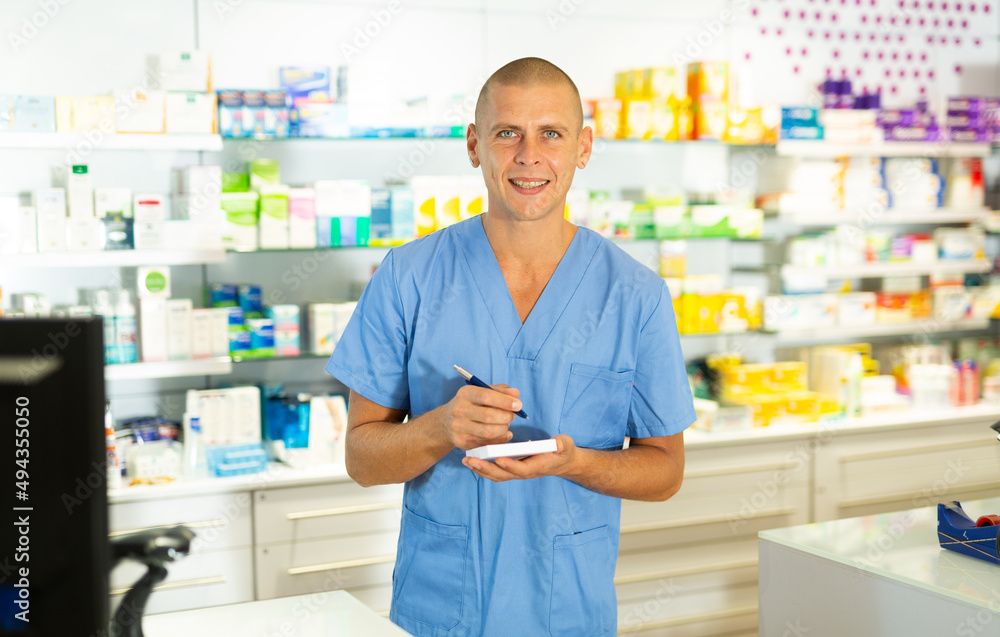 Positive pharmacist makes notes on a notebook in the sales area of a pharmacy