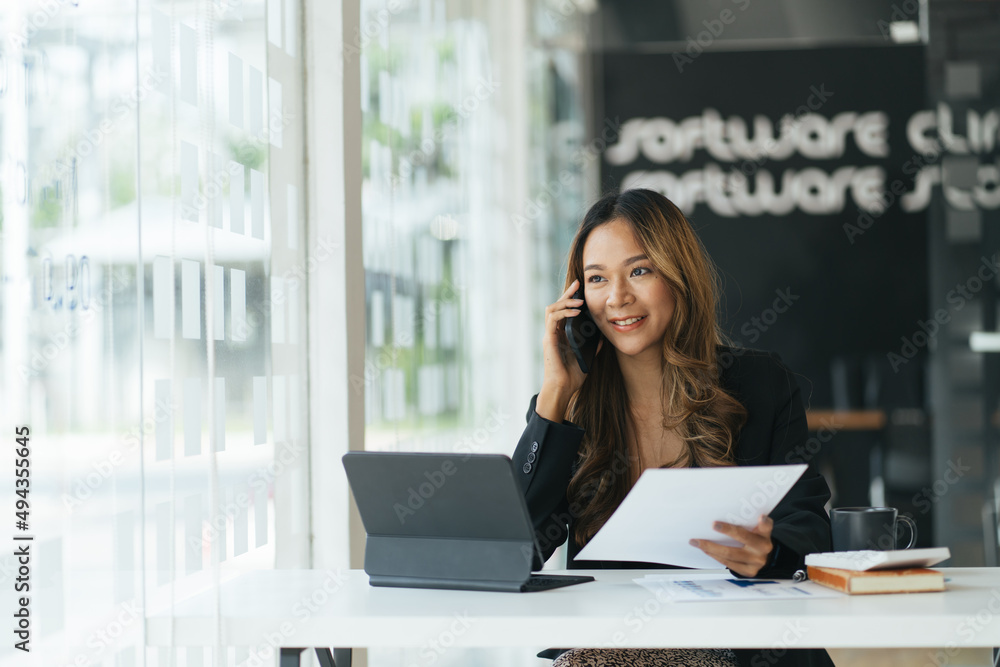 Happy young asian woman talking on the mobile phone and smiling while sitting at her working place in office. Happy young asian woman talking on the mobile phone and smiling while sitting at her working place in office.