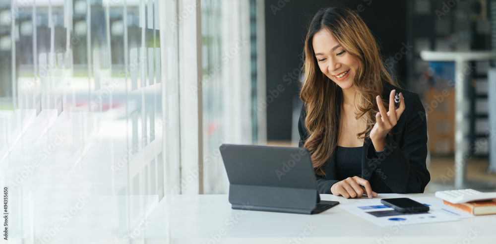 Happy young Asian woman sitting at desk at work and using laptop computer for video call Happy young Asian woman sitting at desk at work and using laptop computer for video call