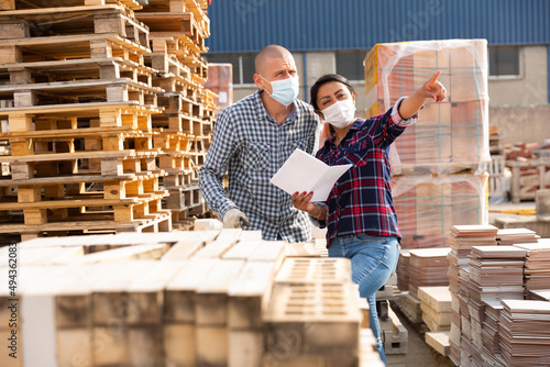 Obraz na plátně Couple of wokers in protective face masks checking order list at hardware store