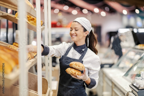 Foto A happy bakery department saleswoman arrange fresh pastry on shelves in supermarket