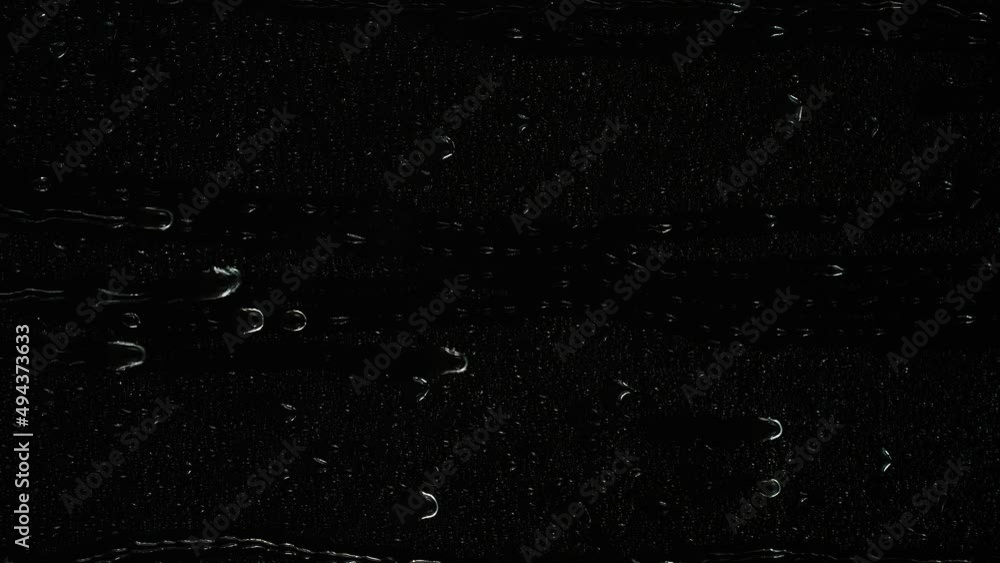 Closeup water rainfall, rain drops falling on window glass over black background Closeup water rainfall, rain drops falling on window glass over black background