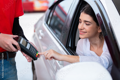 Woman in car paying card reader payment terminal after refuel car ​spending instead of cash with man service employee at gas station. petrol business finance energy concept. photo