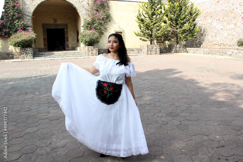 Young teenager woman wears a white regional Mexican dress with black embroidered detail traditional from the state of Veracruz Mexico proud of her culture ready to dance
