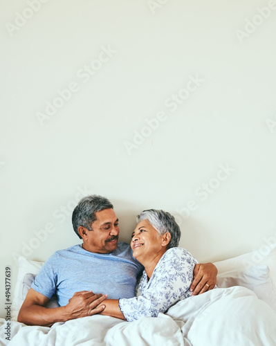 We havent left each others sight since I could remember. Shot of a relaxed mature couple lying in bed together at home in during the morning hours. photo