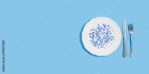 White plate full of microplastics on blue background with copy space. Plastic pollution concept, global ocean pollution ecology problem, microplastic particles in water and food, top view
