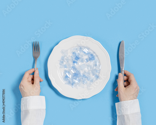 Plate with microplastics as food on blue background. Plastic pollution concept, global ocean pollution ecology problem, microplastic particles in water and food, top view, flat lay, minimal