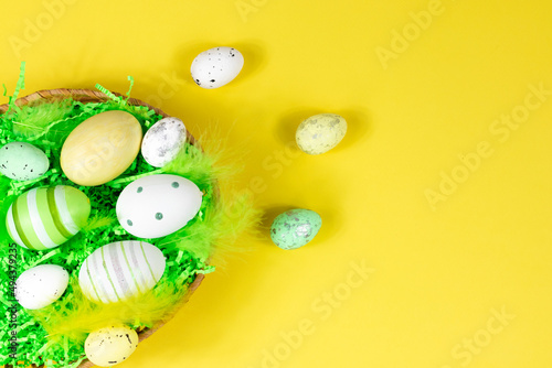 Easter nest with eggs and feathers on a yellow background. View from above. Place for text, lettering. Easter concept.