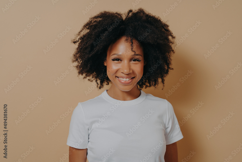 Portrait of cheerful dark skinned woman expressing happiness while standing on beige background Portrait of cheerful dark skinned woman expressing happiness while standing on beige background