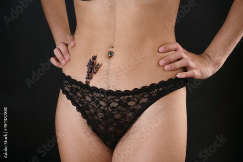 Woman has small lavender flowers sticking out from under her pants, mimicking extra hair. Laser hair removal and shaving with razor. Conceptual shot about women's issues. Proper self care on black photo