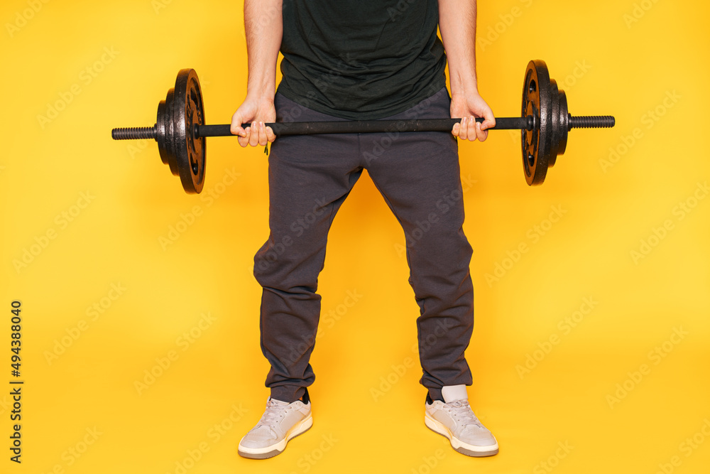 Guy holds barbell in his hands against yellow background. Guy holds barbell in his hands against yellow background.