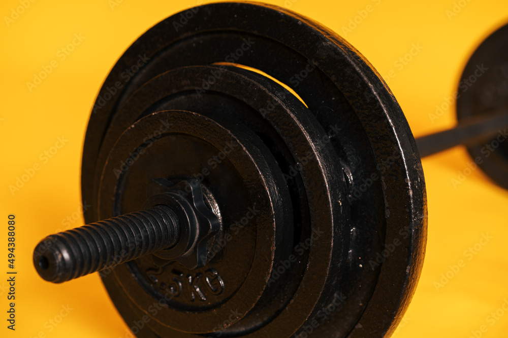 Close-up black barbell against yellow background. Close-up black barbell against yellow background.