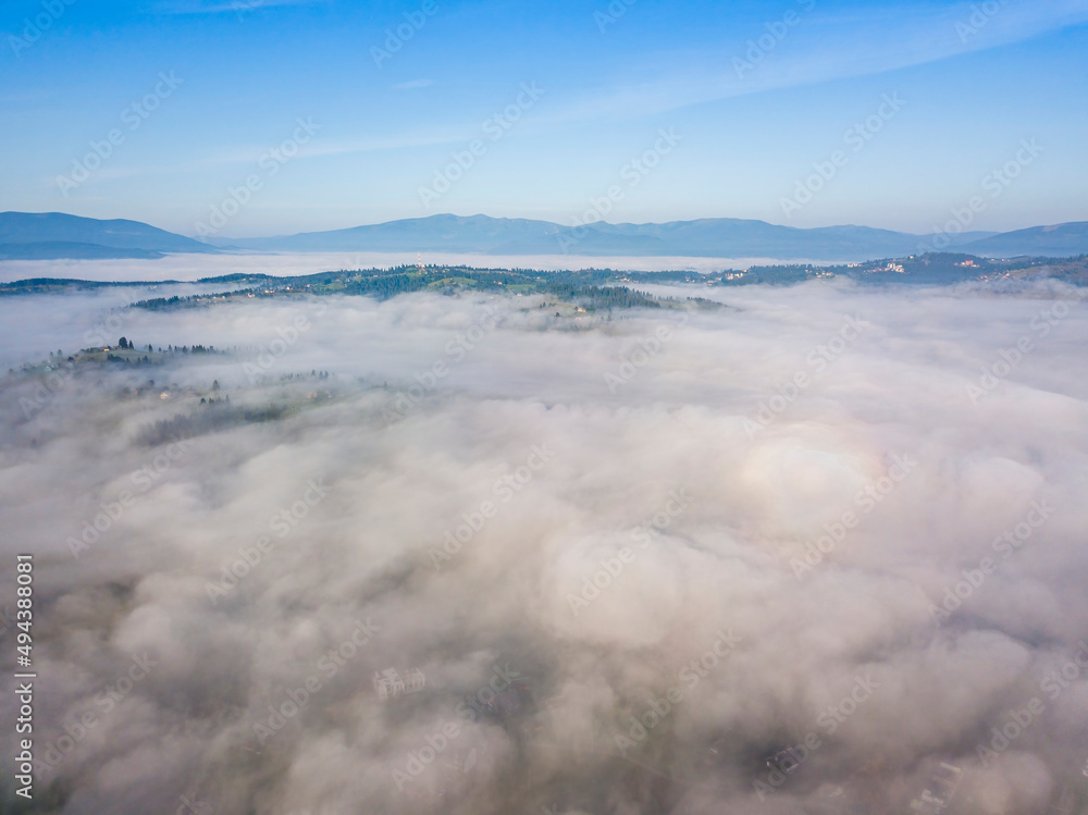 Flight over fog in Ukrainian Carpathians in summer. Mountains on the horizon. Aerial drone view.