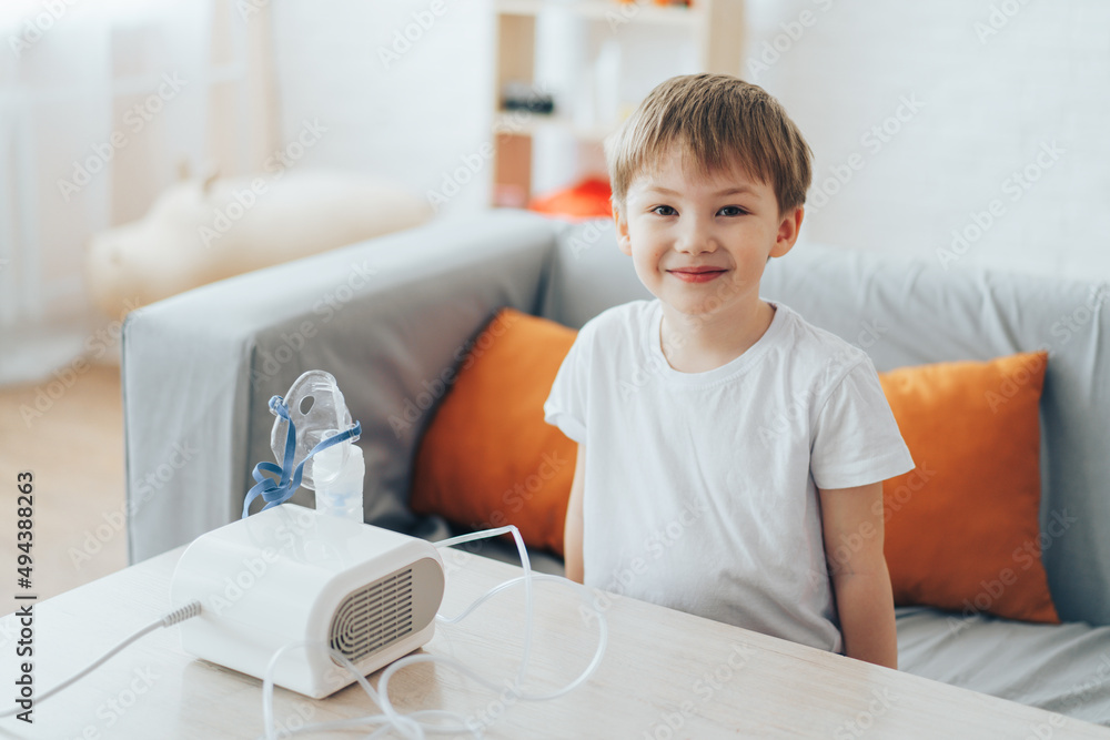 Fototapeta premium Little boy sitting on the couch in front of the nebulizer.
