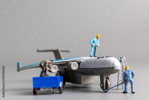 Miniature people worker team checking and repairing airplane on gray background 