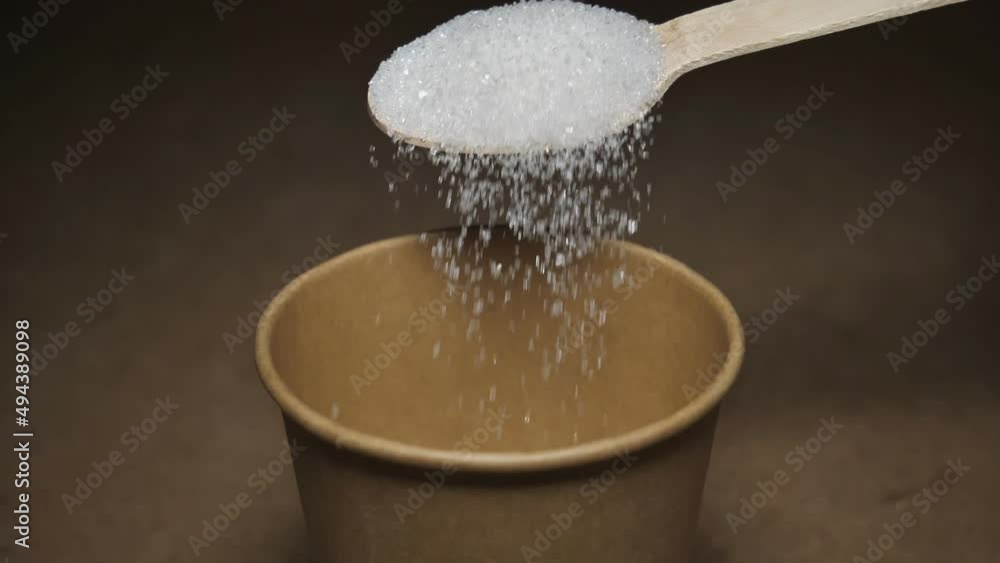 sugar falls from a wooden spoon into a paper glass on a gray background. slow motion video. close-up. Unhealthy diet, diabetes, obesity sugar falls from a wooden spoon into a paper glass on a gray background. slow motion video. close-up. Unhealthy diet, diabetes, obesity