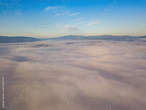 Flight over fog in Ukrainian Carpathians in summer. A thick layer of fog covers the mountains with a solid carpet. Mountains on the horizon. Aerial drone view.