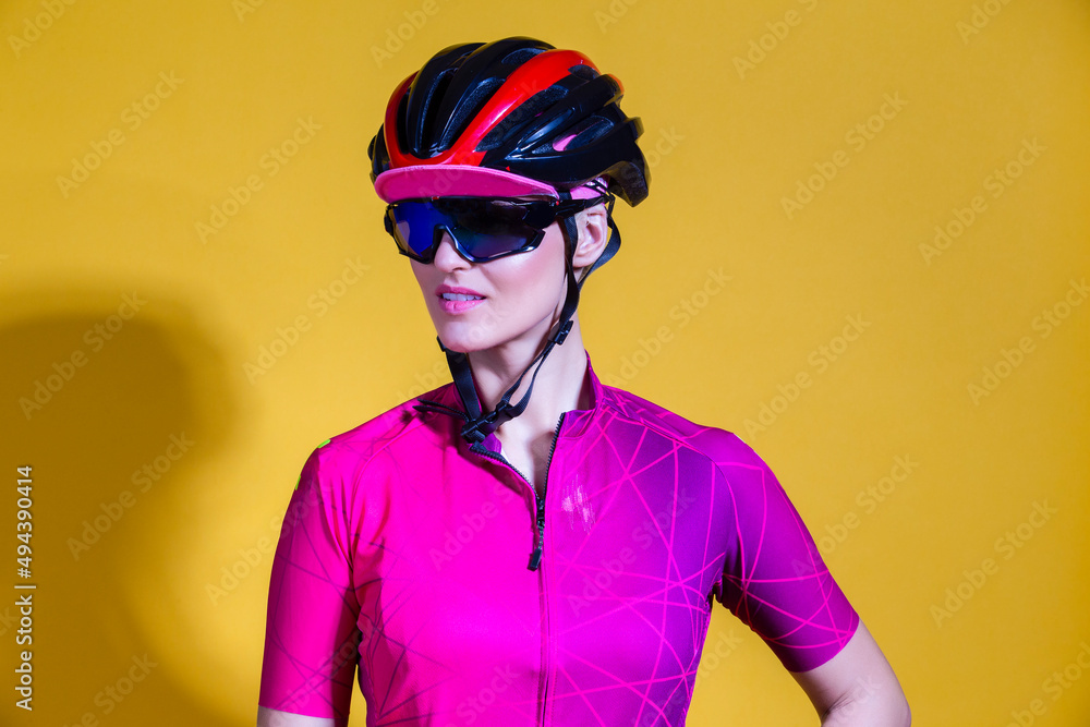 Sport Cycling Concepts. Winsome Positive Female Road Cyclist in Professional Short Sleeve Jersey Outfit Posing Against Yellow Background. Sport Cycling Concepts. Winsome Positive Female Road Cyclist in Professional Short Sleeve Jersey Outfit Posing Against Yellow Background.