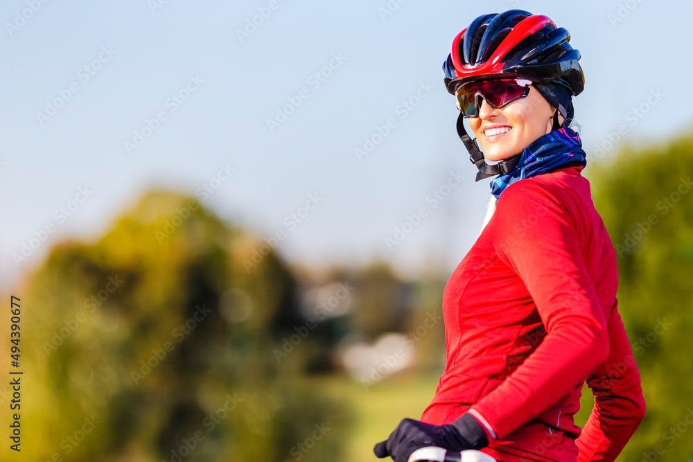 Road Cycling Ideas. Winsome Caucasian Female Cyclist In Warm Outfit Posing On Road Bike While Smiling Turned Backwards Outdoors Against Autumn Background. Road Cycling Ideas. Winsome Caucasian Female Cyclist In Warm Outfit Posing On Road Bike While Smiling Turned Backwards Outdoors Against Autumn Background.