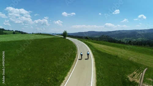 Aerial view of mountain empty road and two bikers cycling. In the background wide mountain range and epic alpine view. Concept: Vacations in the mountains, traveling on a bike