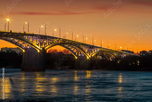 Bridge at sunset, with yellow illumination, frozen river, ice. © Nikita