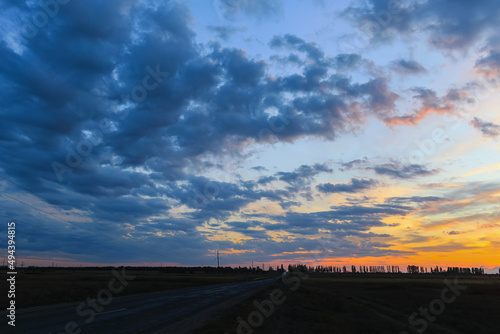 A beautiful bright sunset in the countryside. The orange-blue sky looms over the country road and fields.
