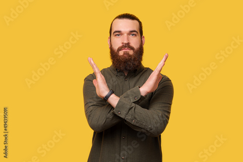 Serious bearded man is showing stop or x gesture made with arms.