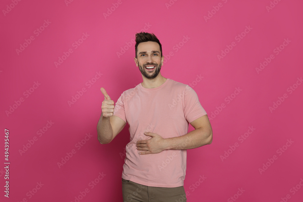 Happy man touching his belly and showing thumb up on pink background. Concept of healthy stomach Happy man touching his belly and showing thumb up on pink background. Concept of healthy stomach