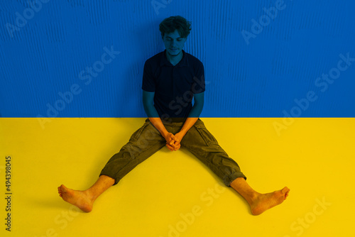 Фототапет A young man is sitting on the floor in the colors of the Ukrainian flag