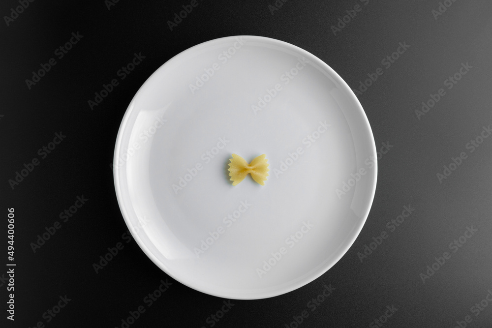 Raw pasta farfalle on plate on black background.