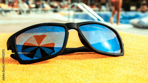 Black sunglasses summer background. Beach pool equipment with travel sunglasses on yellow holiday towel. Sun glasses near swimming pool, holiday concept.