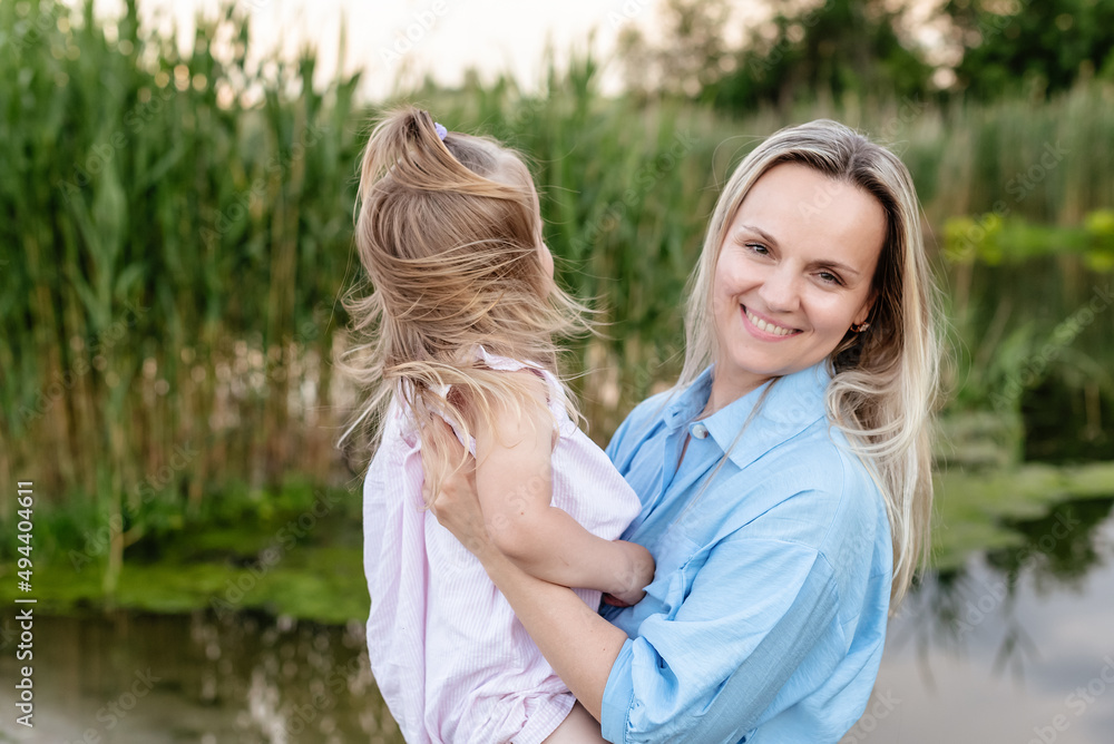 Caucasian Mother with a toddler daughter hugging enjoying outdoors by the river or lake in summer. Happy family portrait. Spending family time together. Single parent