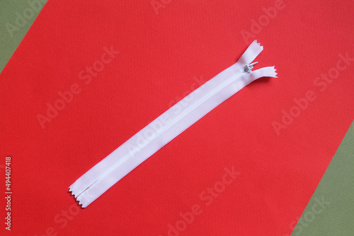 A white short zipper for clothes lies on a red-green surface, close-up, top view. Sewing accessory. Accessories.