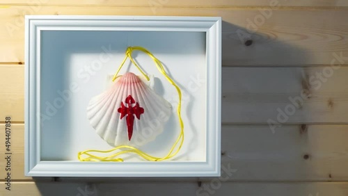 wooden frame with pilgrim shell of the Camino de Santiago  on room wall illuminated by light from one window , souvenir of  trip walking  to Compostela, video hd footage photo