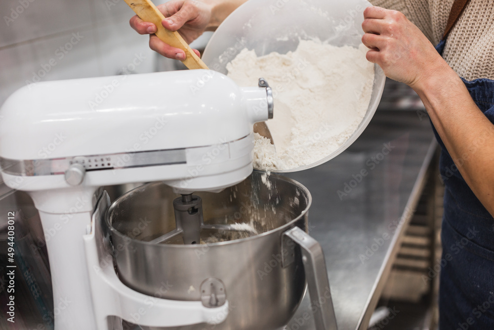 Pastry chef pouring flour with help of wooden spoon to blender