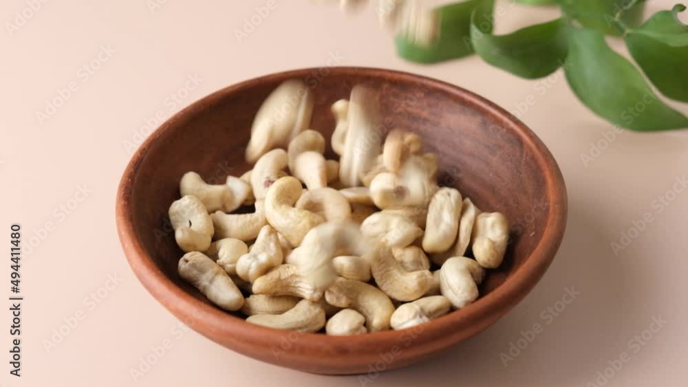 Cashew nuts in a bowl on beige background. Slow motion cashews falling Cashew nuts in a bowl on beige background. Slow motion cashews falling