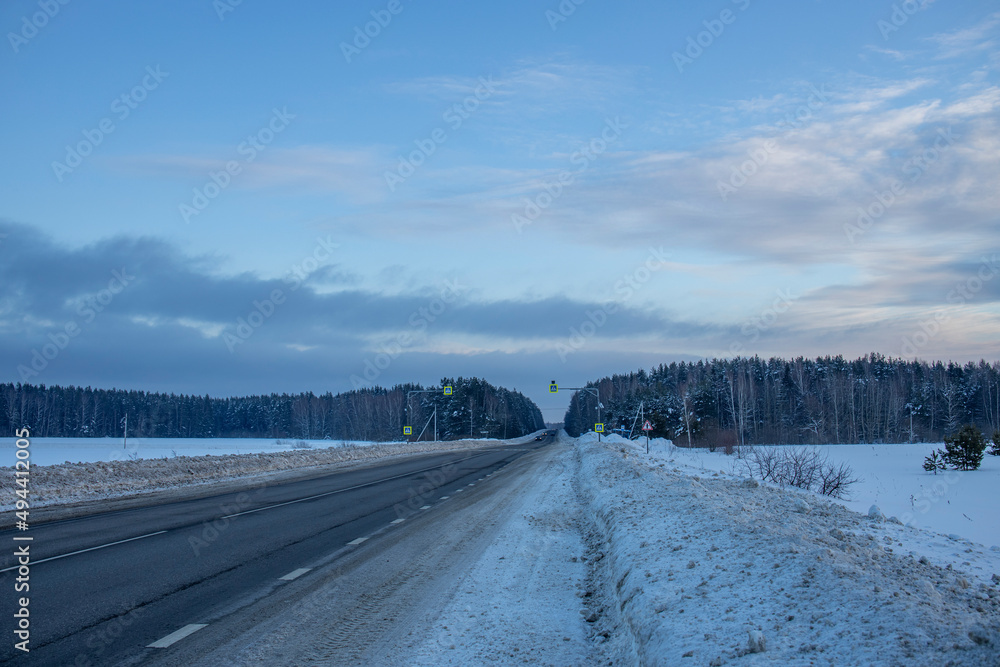 Obraz premium Winter evening landscape, road in the foreground. Sunset sky over the horizon.
