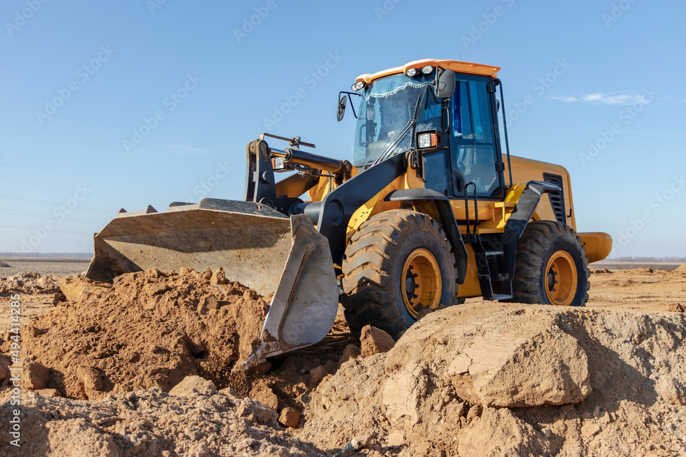 Bulldozer or loader moves the earth at the construction site against the blue sky. An earthmoving machine is leveling the site. Construction heavy equipment for earthworks.