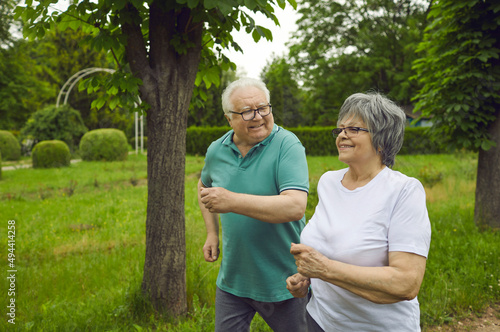 Happy active senior couple enjoying jogging workout on warm summer morning. Energetic old husband and wife running along green park path together. Sport, fitness and healthy lifestyle concept