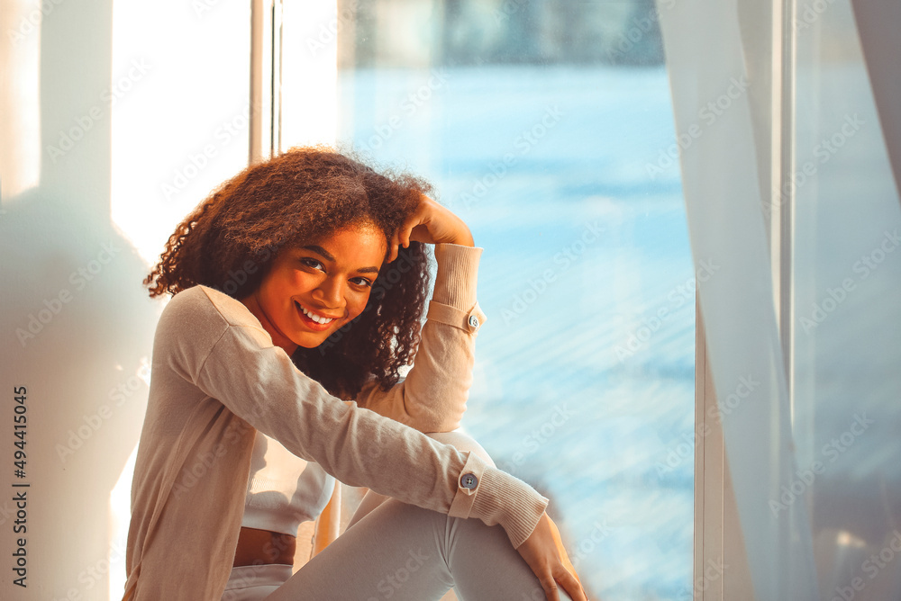 Pleased relaxed African American ethnicity girl in homewear sitting on  windowsill Stock Photo | Adobe Stock