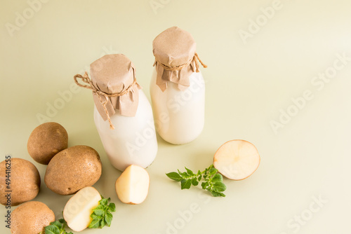 two bottles of environmentally friendly potato milk from all types of plant-based milk on a beige background with potato tubers.