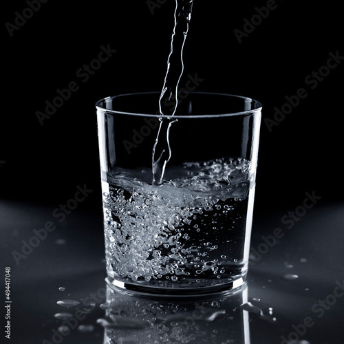 Vaso de crsital con chorro de agua sobre fondo negro photo
