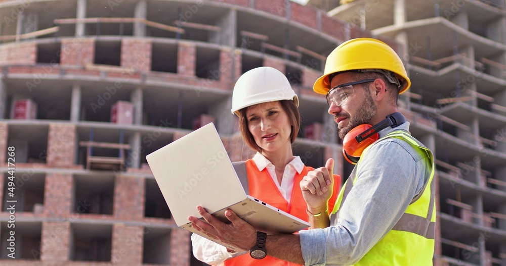 Builders, foreman and female architect standing in front of construction site and look at the lap top, discussing their job. The concept of new technologies in construction. Front view. Close up. Builders, foreman and female architect standing in front of construction site and look at the lap top, discussing their job. The concept of new technologies in construction. Front view. Close up.