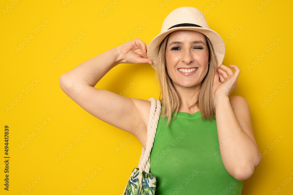 Portrait of a cheerful smiling woman in straw hat with winked eye isolated over yellow background. Portrait of a cheerful smiling woman in straw hat with winked eye isolated over yellow background.