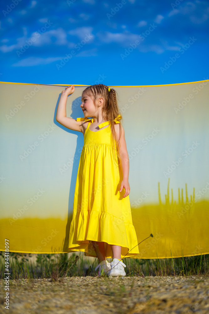 Obraz premium Ukrainian girl 7 years old, she is a patriot of Ukraine, dressed in a yellow dress against a blue sky. Blue sky. Sunny day. Free Ukrainian child. Child symbol of Ukraine