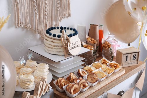 Baby shower party. Different delicious treats on wooden table and decor near light wall